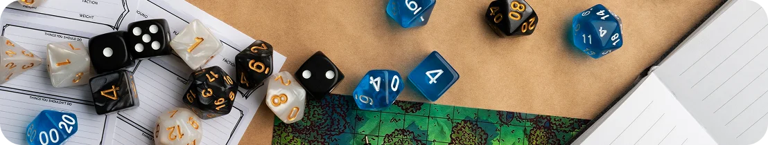 Kostky a herní prvky stolní RPG nebo deskové hry položené vedle mapy a poznámkového bloku.